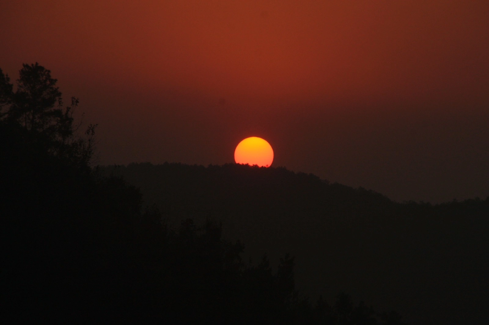 The sun setting behind a quiet wooded ridge in Himachal Pradesh